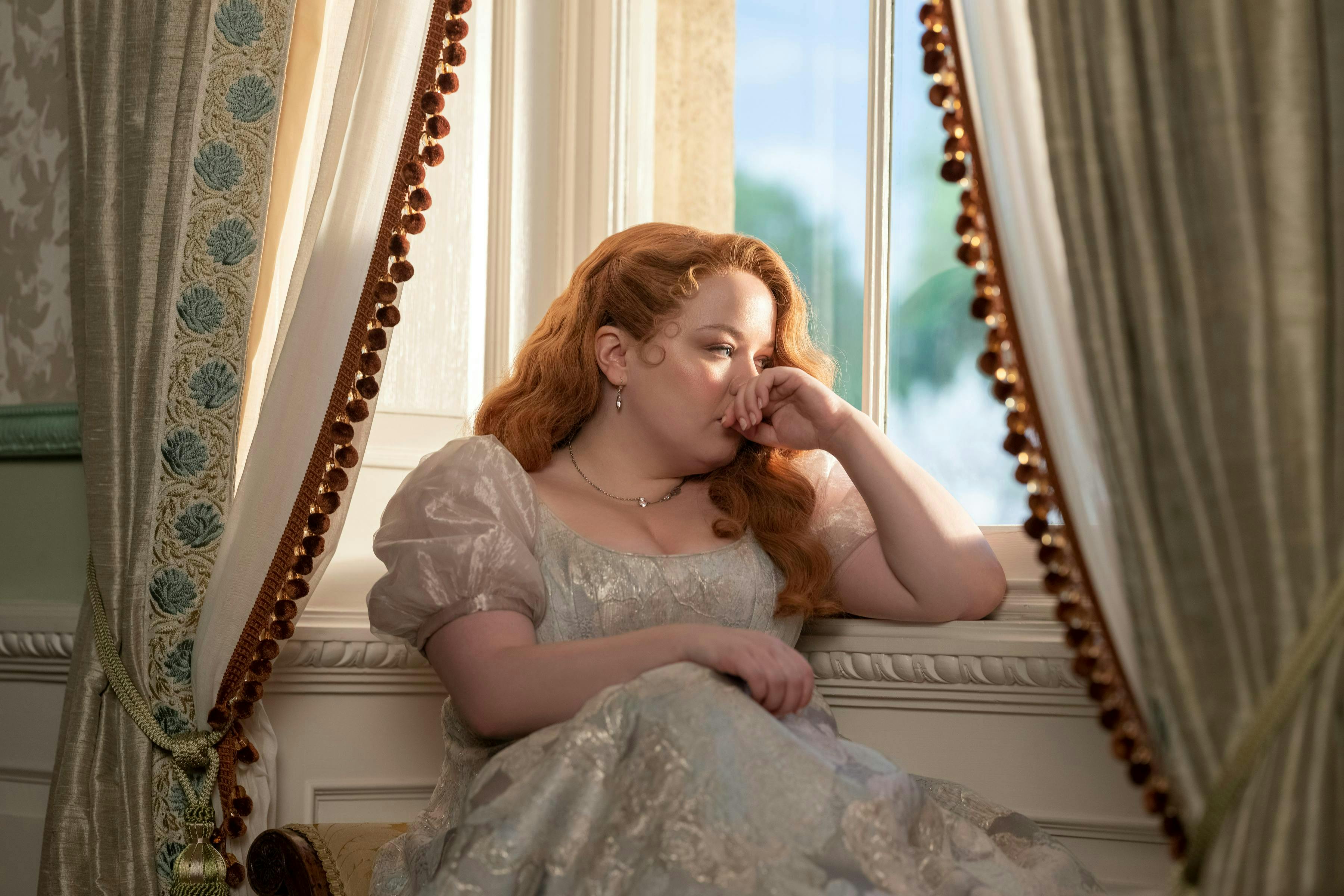 Penelope Featherington sitting down near a window.