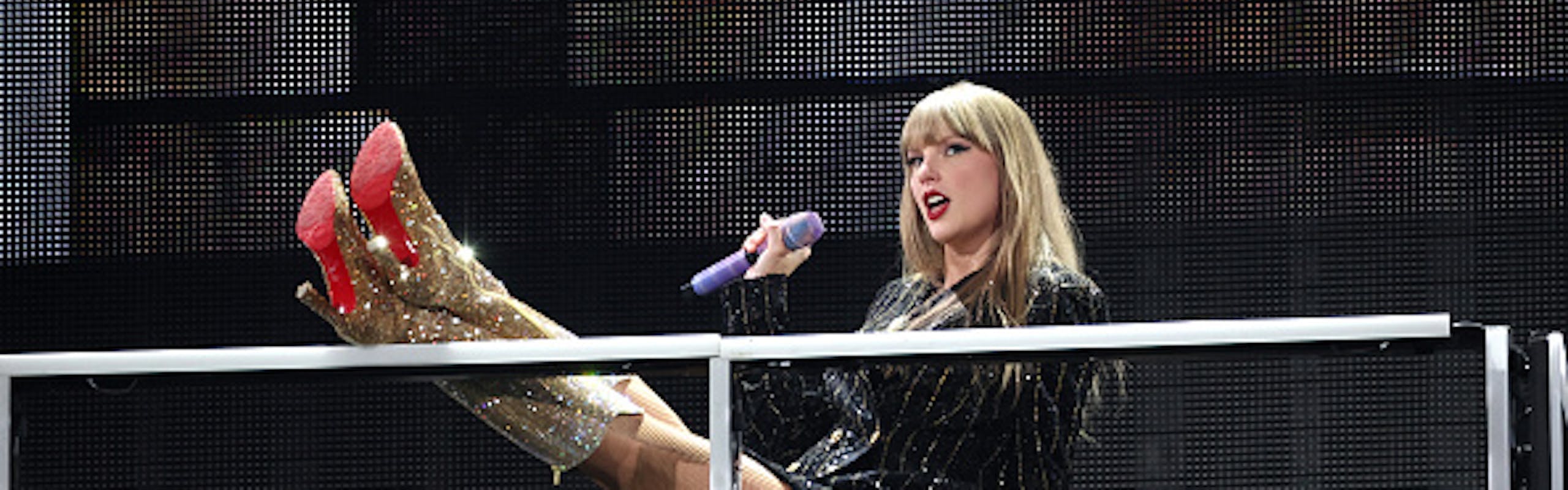Taylor Swift performing in gold boots and a striped sparkly blazer in Paris for The Eras Tour. Getty Images.