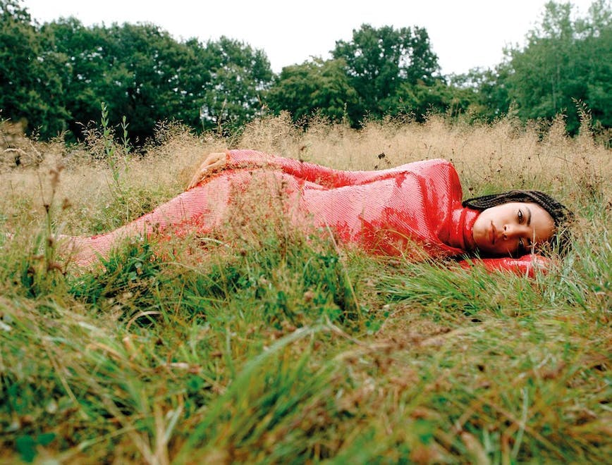 Elodie wears a sequin dress in the grass with trees and the sky above her