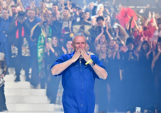Jean Paul Gaultier blowing a kiss as he walks down the runway with a crowd behind him