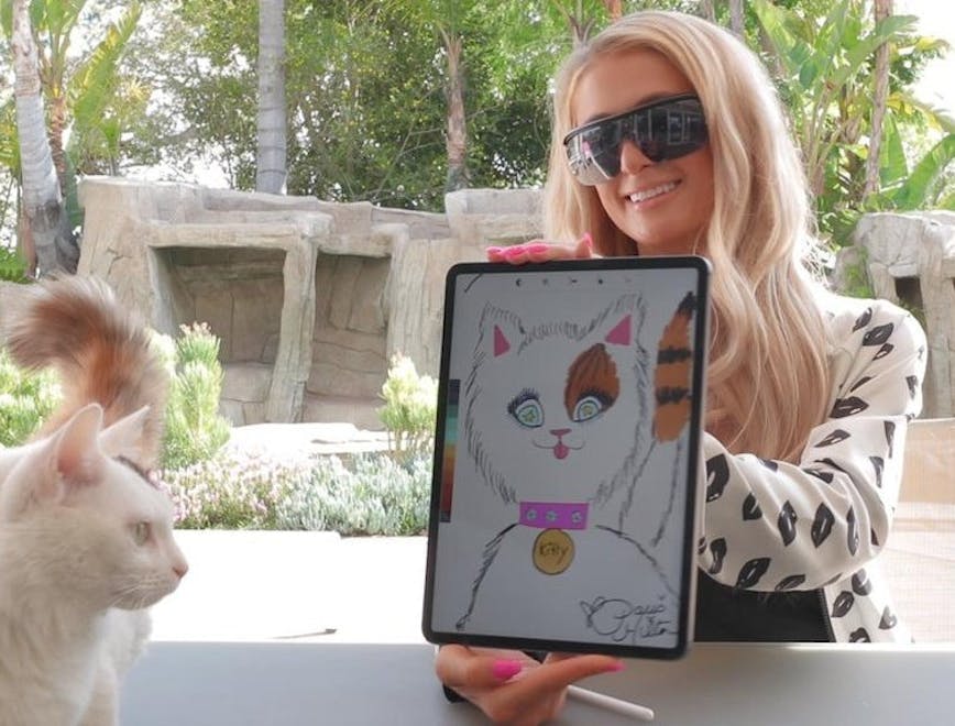 Paris Hilton holding up an iPad with a drawing of a cat on it.