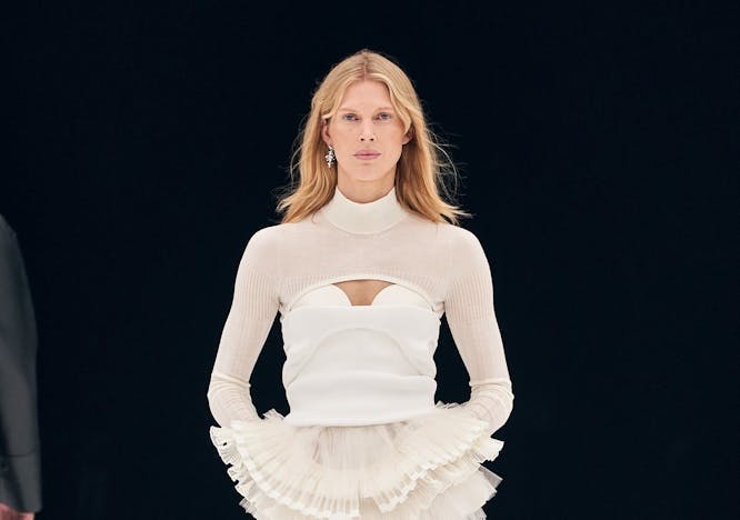 Model in white top and cream drop shoulder cropped sweater and cream maxi skirt with ruffle and cut-out detailing.