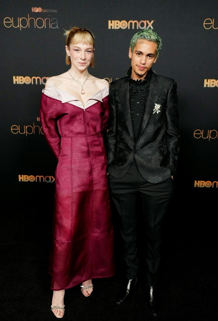 Hunter Schafer in a long red dress next to Dominic Fike in a black suit.