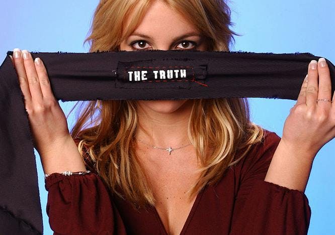 Britney Spears holds a long strip of fabric in front of her face that reads "The truth" in front of a blue background