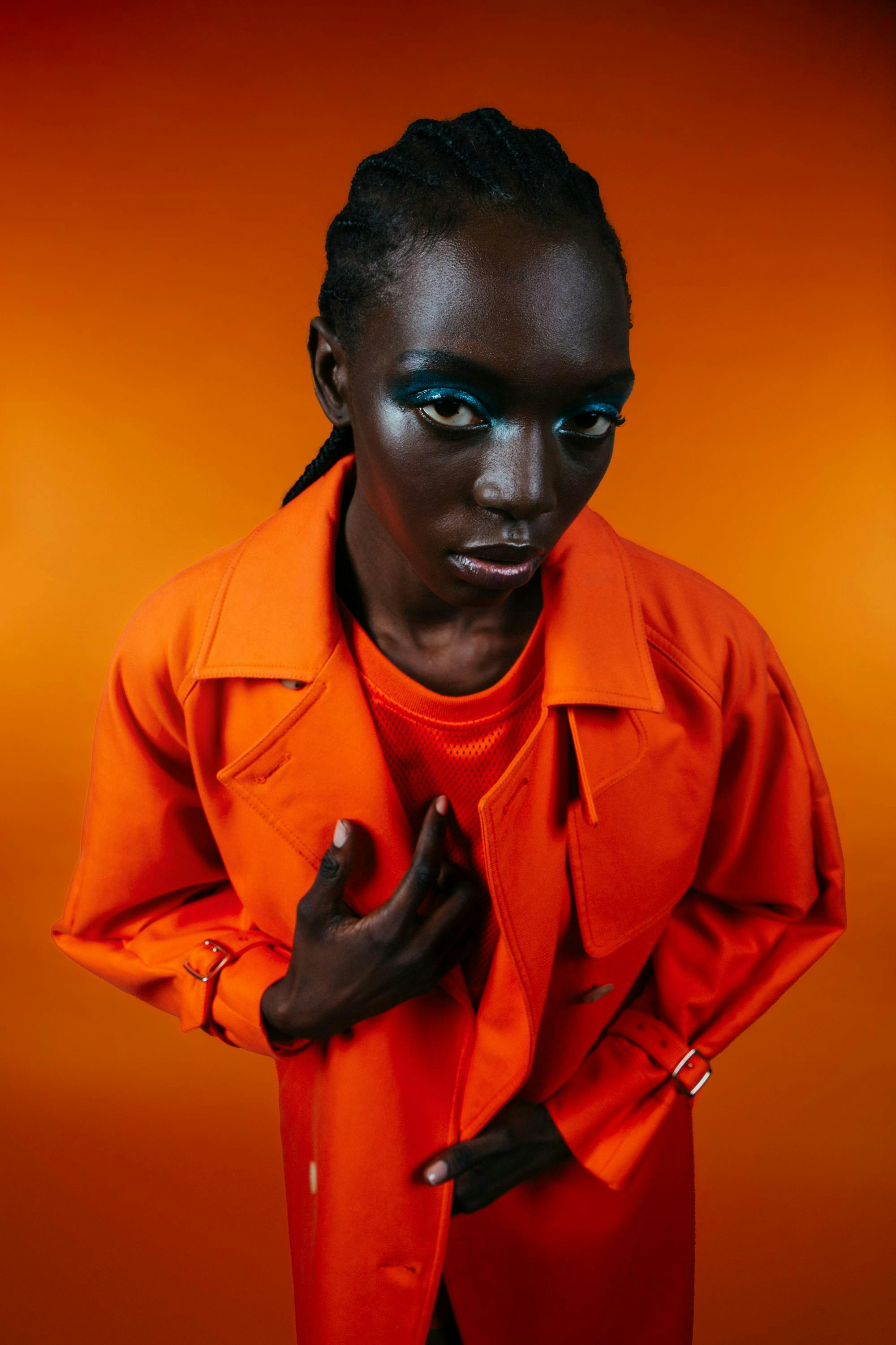 model with blue eyeshadow wearing a bright orange blazer, shirt, and watch for monochromatic citrus orange outfit.
