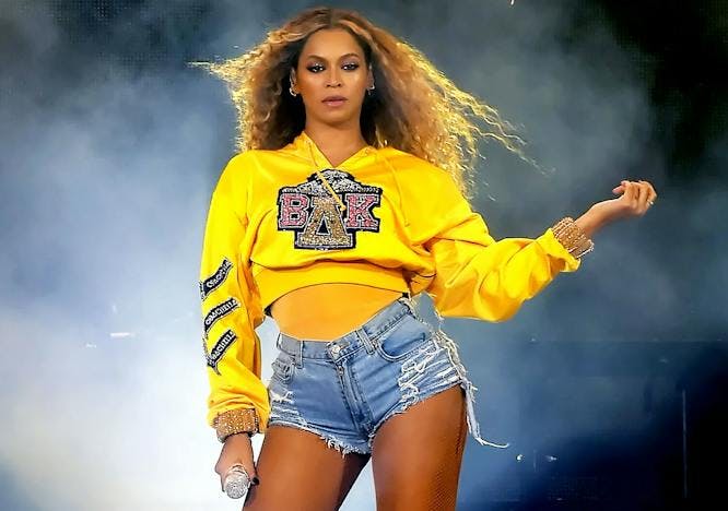 Beyonce on stage in denim shirts and a sequined yellow sweatshirt holding a microphone with her other hand out
