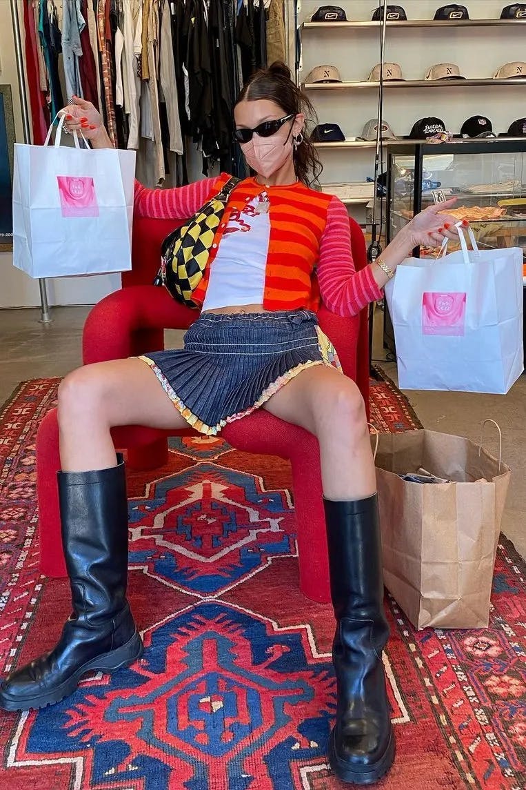 Bella Hadid holding two shopping bags sitting in a chair