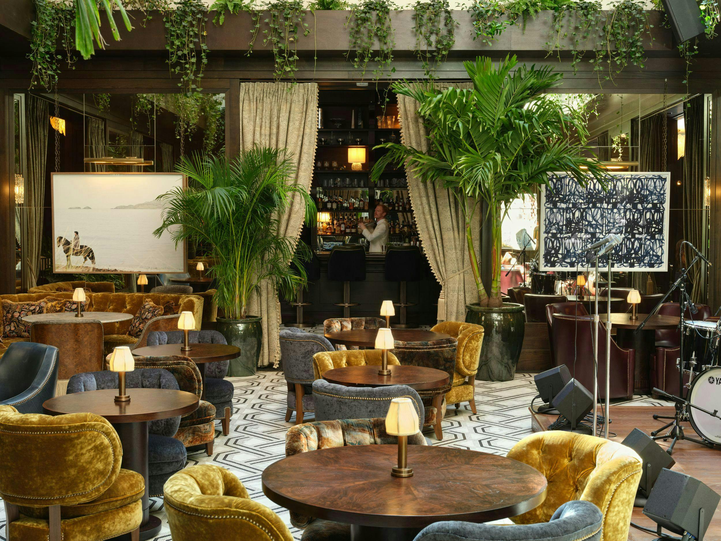 The Ned NoMad hotel is pictured. Tables with yellow chairs and lots of greenery fill the room.