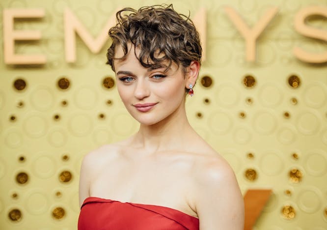 Joey King poses in a red dress behind an Emmy's backdrop. 
