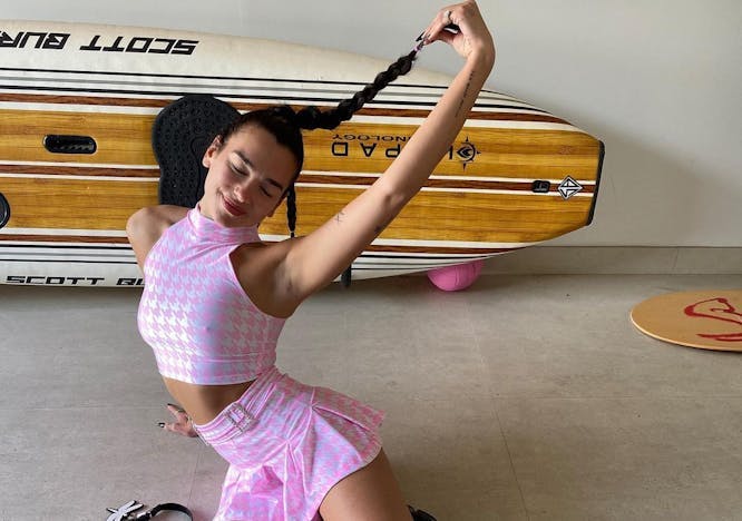 Dua Lipa, the queen of preppy summer trends, poses in a matching pink houndstooth skirt and crop top.
