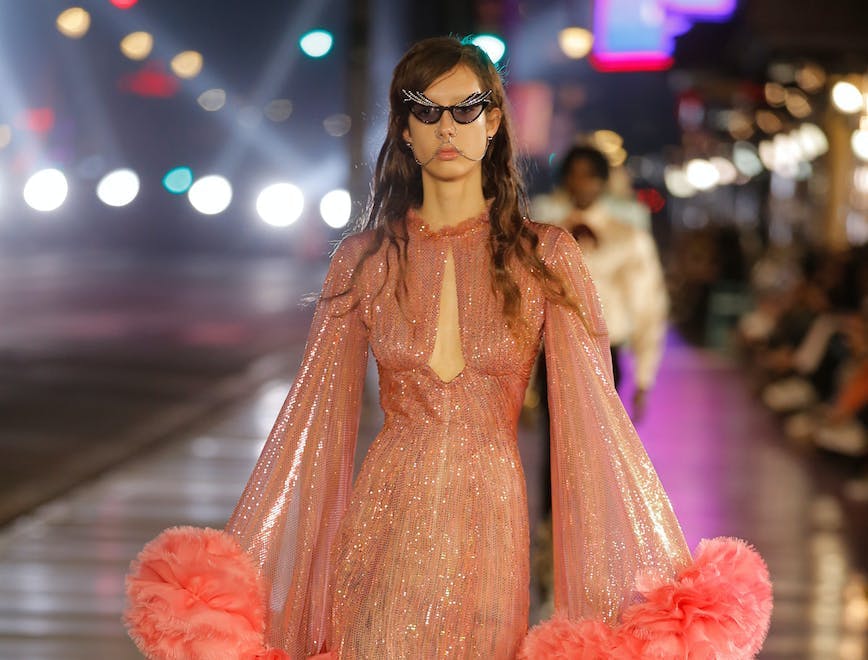 A model in Gucci runway show wearing a salmon shimmery dress with feathery details and black cat eye sunglasses