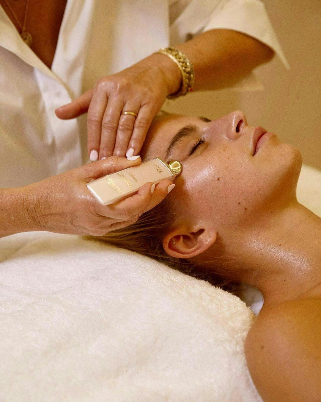 A woman applies a product to another woman receiving a facial. 