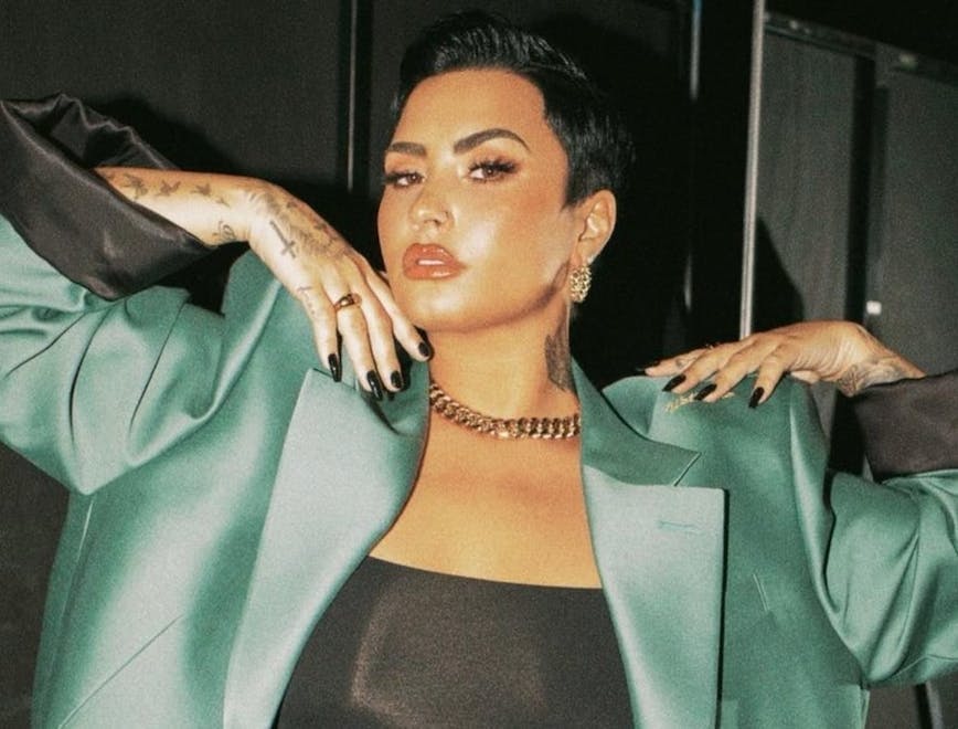 Demi Lovato poses with her arms up, in a green satin suit jacket.