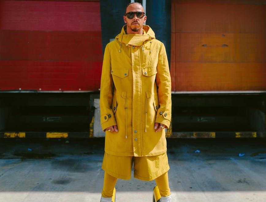 Lewis Hamilton wearing an oversized yellow utility jacket, matching shorts with leggings underneath and white sneakers.