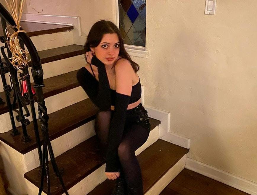 Lizzy McAlpie sits on a staircase and poses for a photo in an all-black outfit.