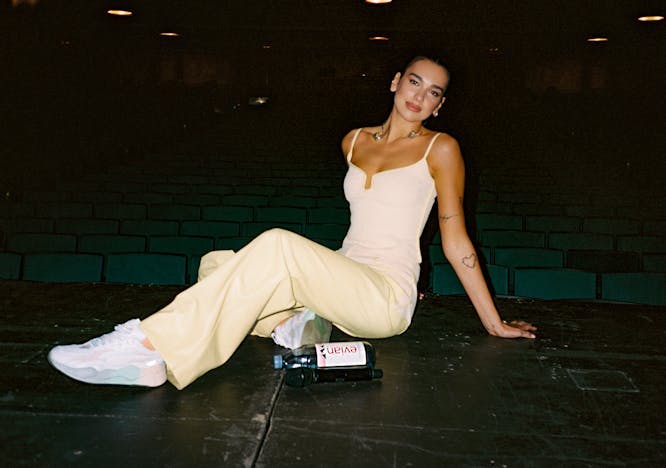 Dua Lipa on stage wearing a pale yellow jumpsuit and white sneakers