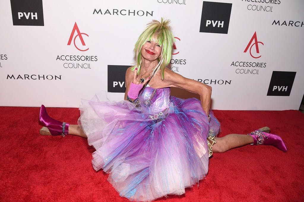 Betsey Johnson doing a split on a red carpet in a puffy purple dress