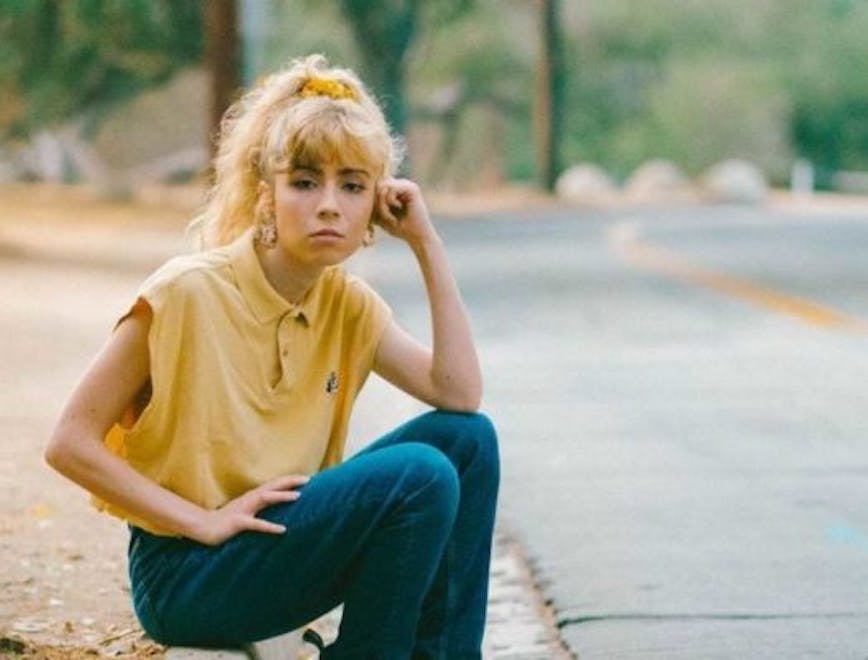 Jennette McCurdy sitting on the sidewalk wearing a yellow shirt