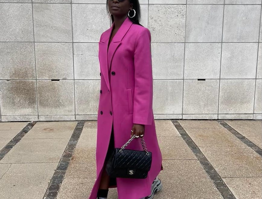 Woman wearing a long hot pink coat, a quilted Chanel bag and chunky sneakers