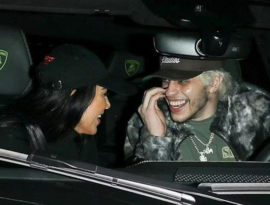 Kim Kardashian and Pete Davidson inside a car at night smiling at one another while Pete drives