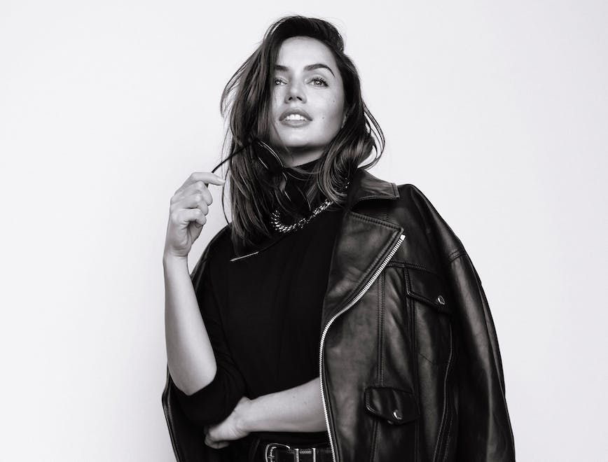 Black and white photo of Ana de Armas wearing a black turtleneck, leather jacket and leather and pants and chain necklace.