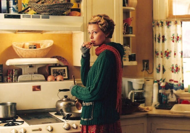 a woman in a green sweater and red scarf cooking in the kitchen