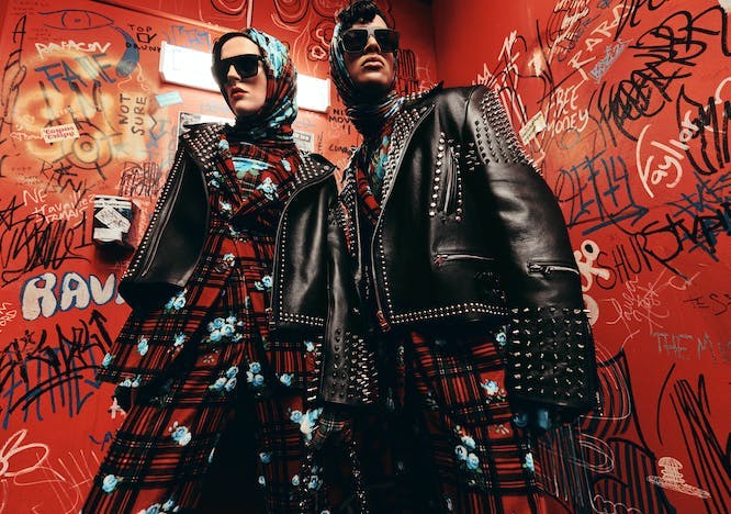Male and female model in matching red and black plaid suits with blue florals and studded leather jackets.