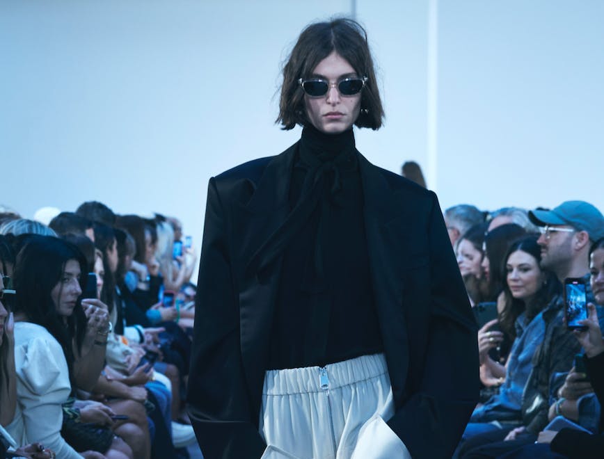 model walking in black blazer, black top, and white pants