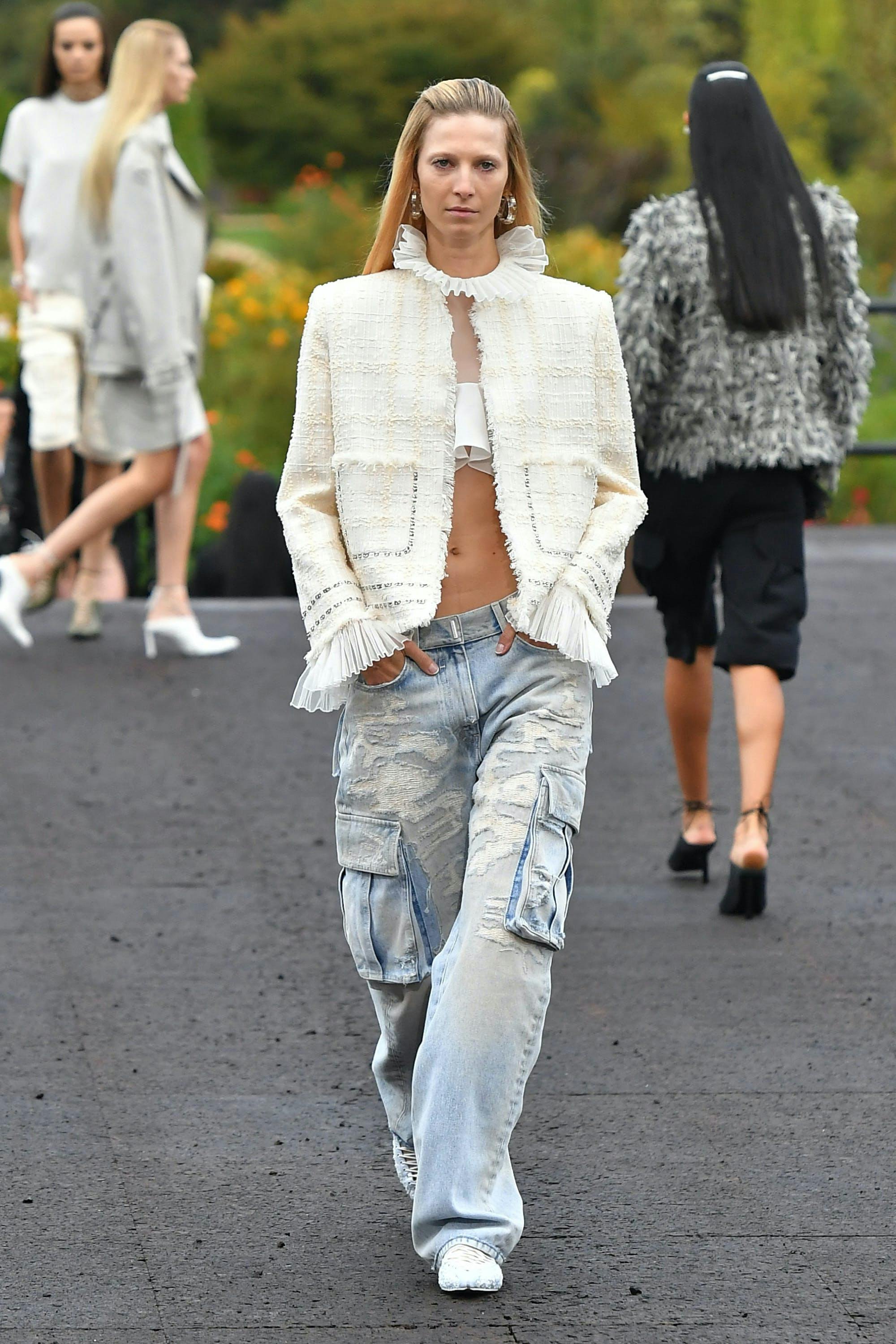 A model in a white jacket and baggy blue jeans.