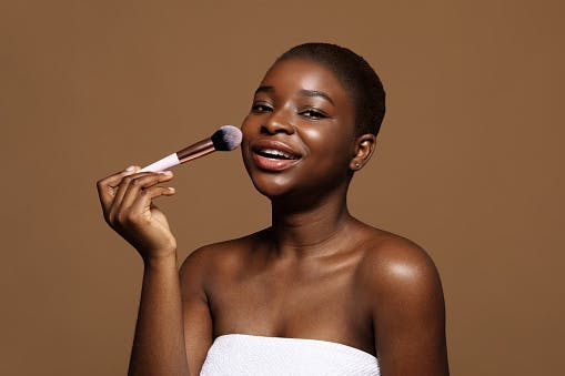 woman holding makeup brush brown background