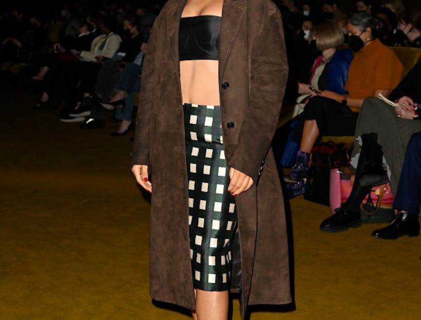 Woman in a black bandeau top, checkered midi skirt, and brown coat.