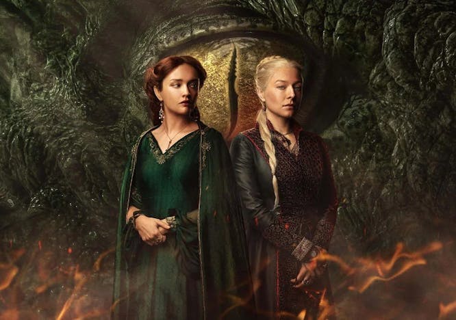 Two women standing next to each other in front of the eye of a dragon.