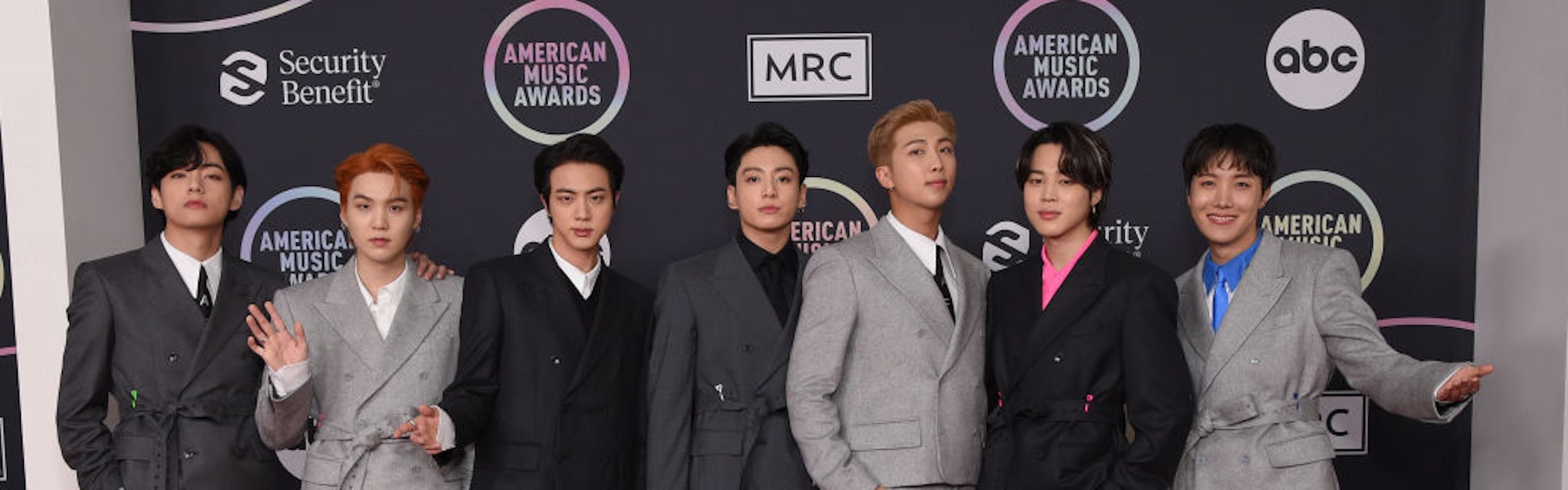 A group of guys in grey and black suits while standing on a red carpet.