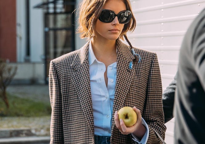 Kaia Gerber in a blazer and blue shirt holding an apple