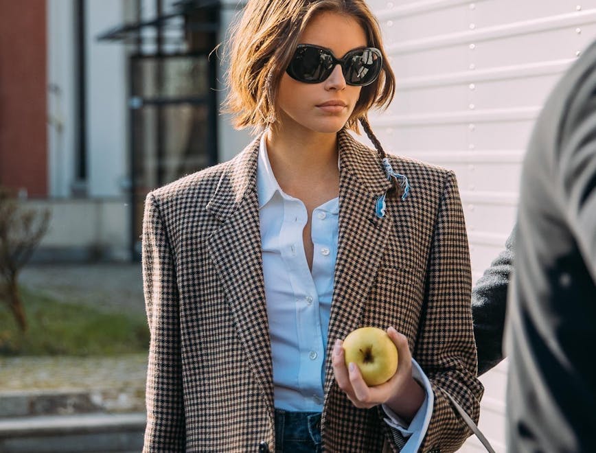 Kaia Gerber in a blazer and blue shirt holding an apple