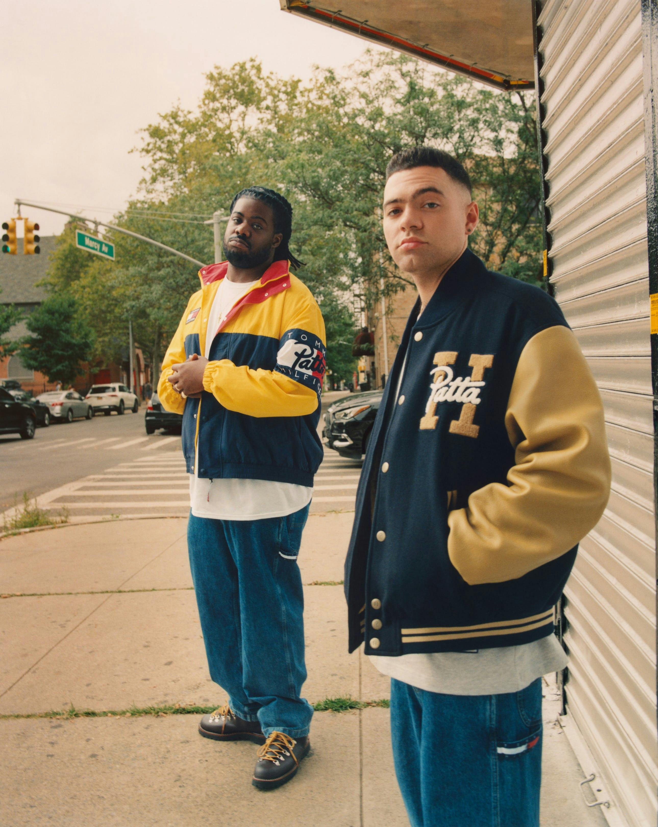 Two men wearing varsity jackets and jeans looking at the camera.