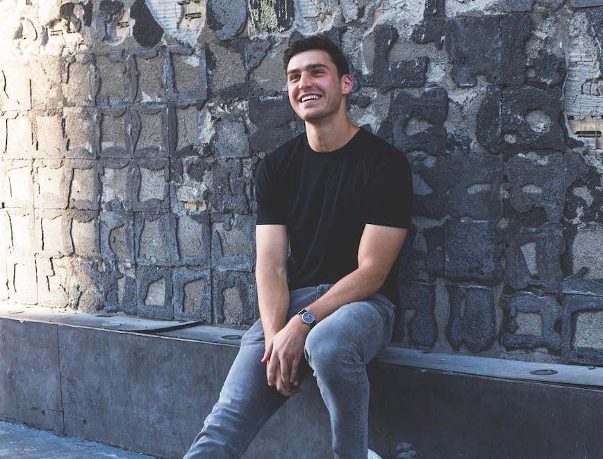 A guy in a black shirt and jeans smiling.