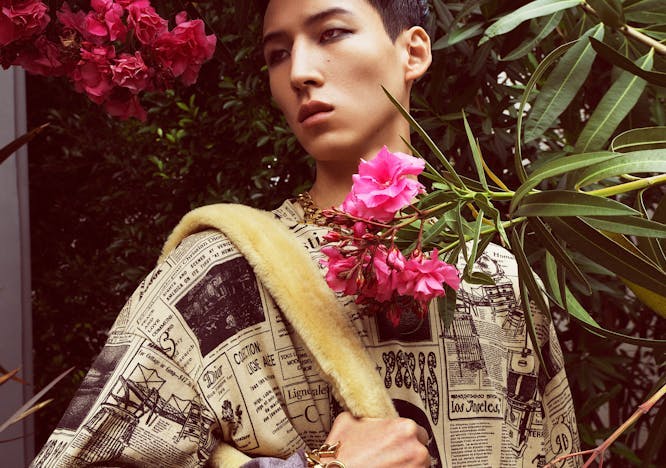 Model wearing newspaper-graphic shirt with yellow bag on garden background