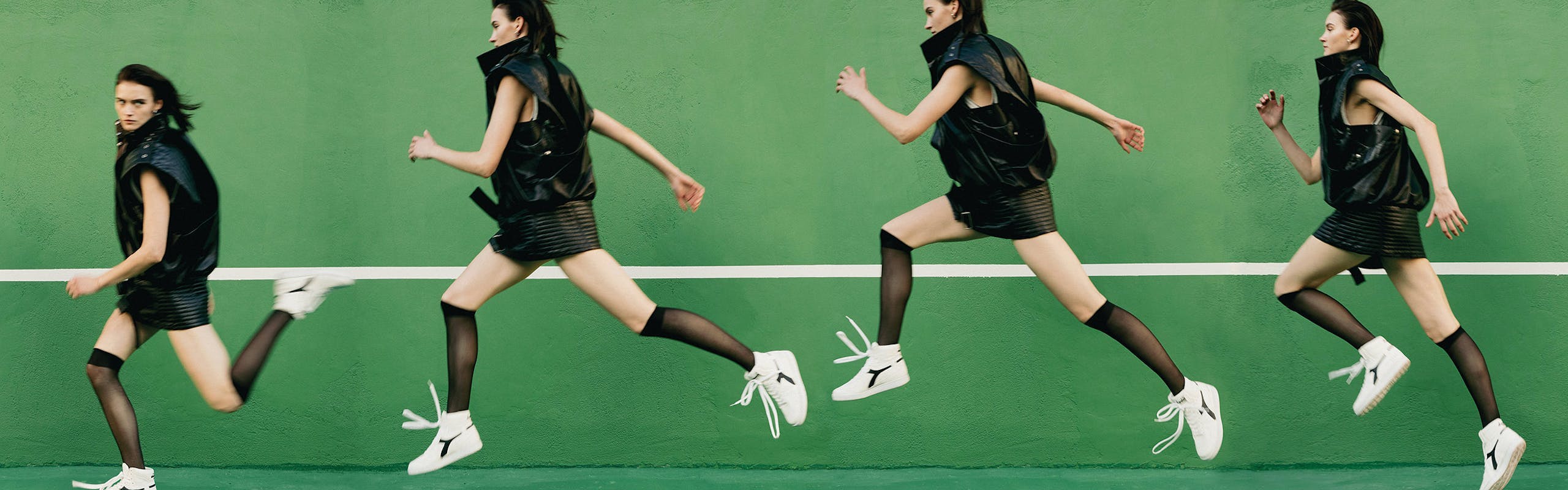 Model wearing a black vest with with a  black dress and white sneakers on a lush green background