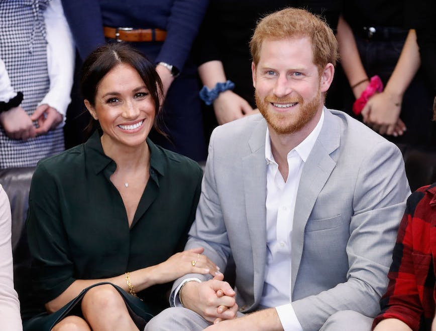 Meghan Markle in a green dress sitting next to Prince Harry in a light grey suit.