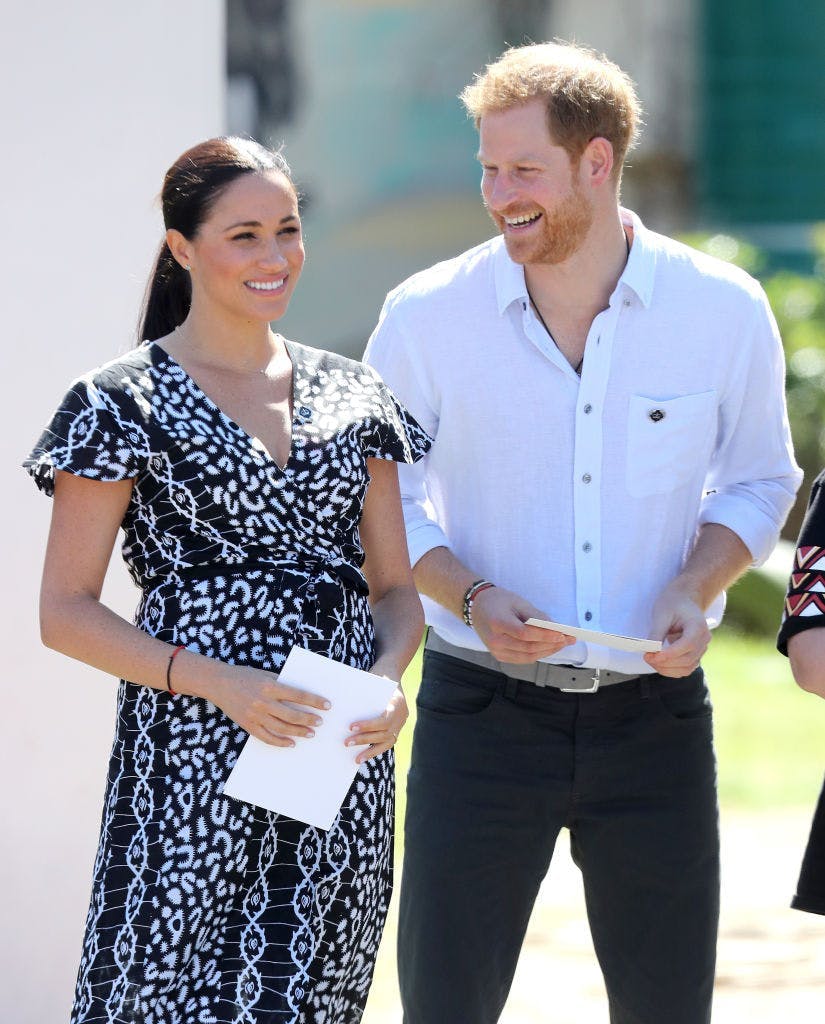 Meghan Markle in a black dress next to Prince Harry in a white dress shirt and dark pants.