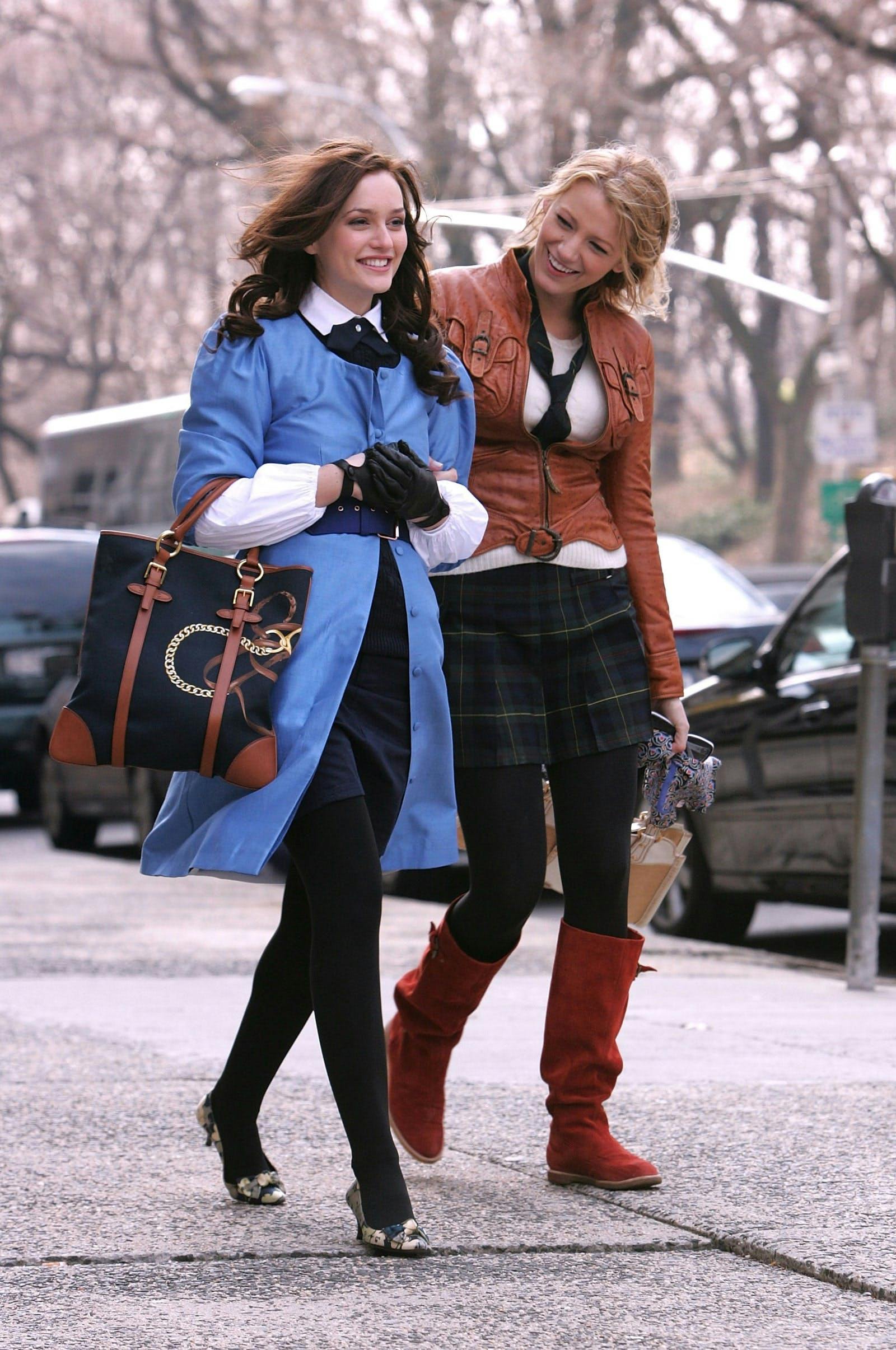 Woman in blue coat and black skirt with woman in brown coat and plaid skirt walking on the street.