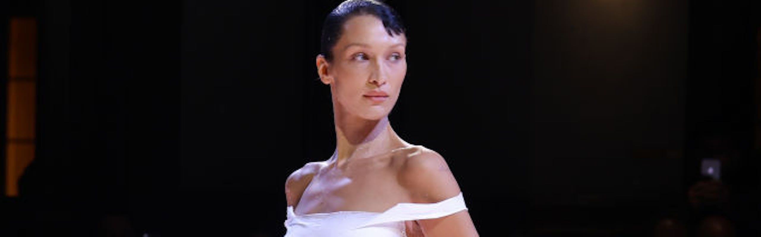 A model in a white dress while posing on the runway.