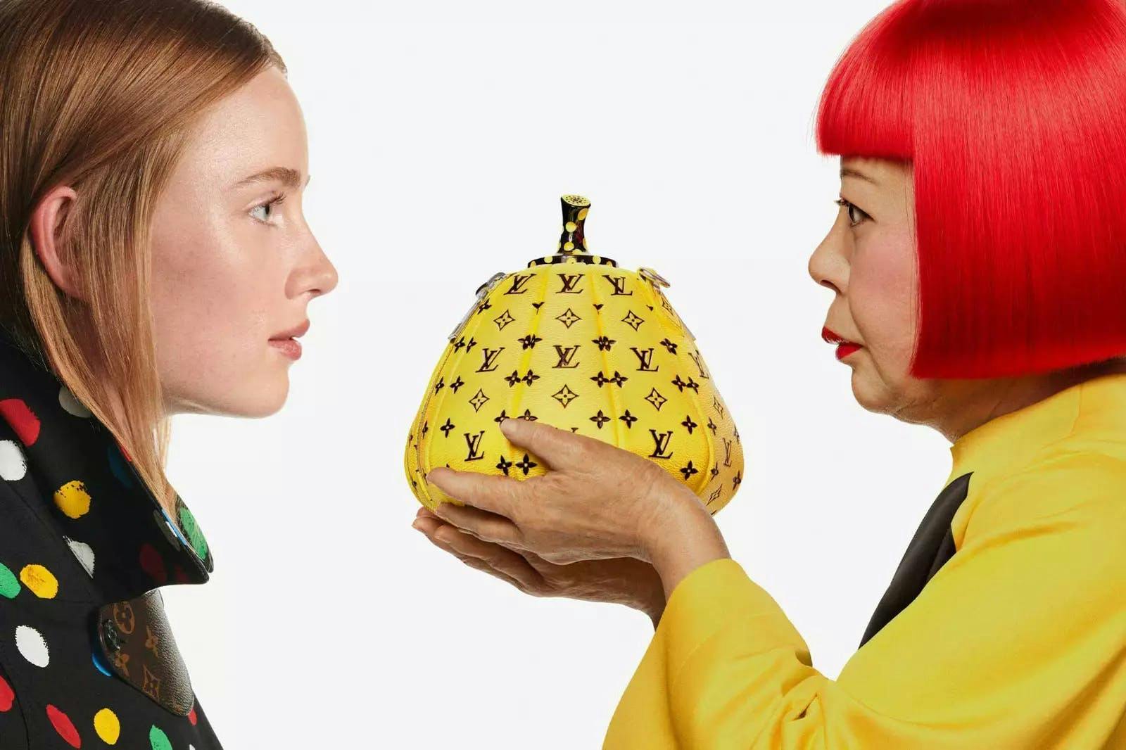 Two women looking at each other against a white backdrop while one woman hold a yellow pear shaped purse.