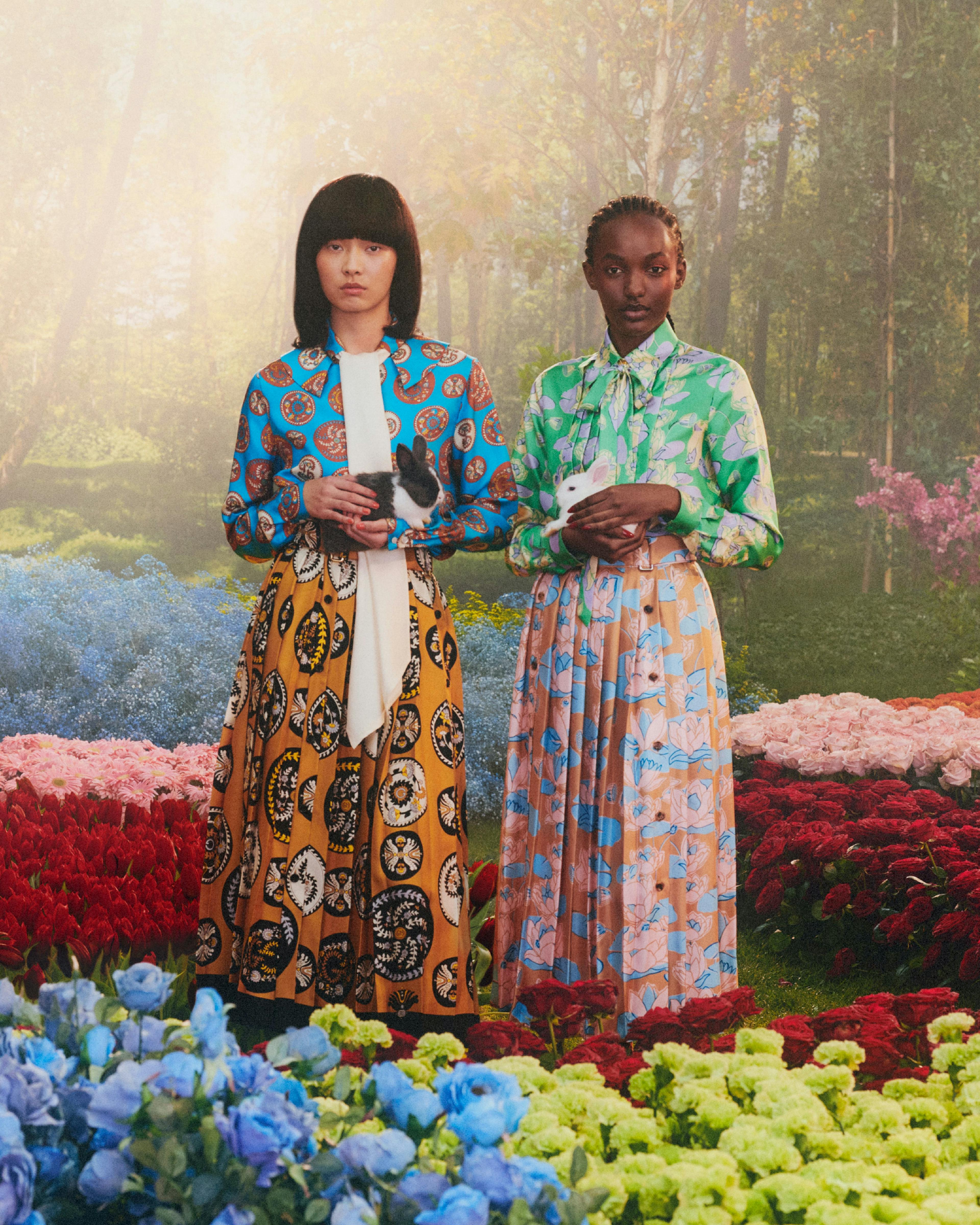 Two models standing in a colorful field holding two bunnies.
