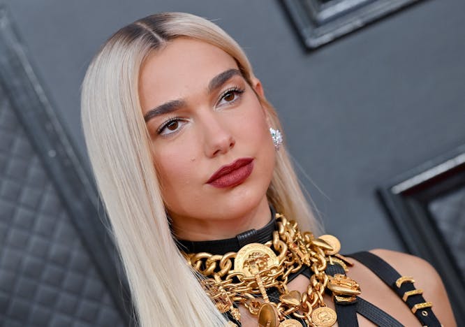 Dua Lipa wearing a layered gold-toned Versace necklace with a pair of oversized earrings.