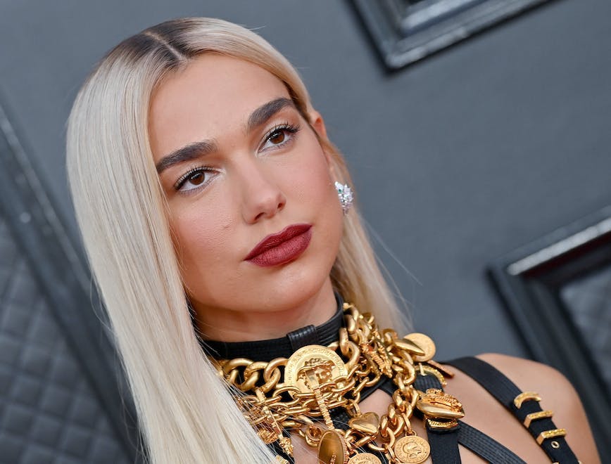 Dua Lipa wearing a layered gold-toned Versace necklace with a pair of oversized earrings.
