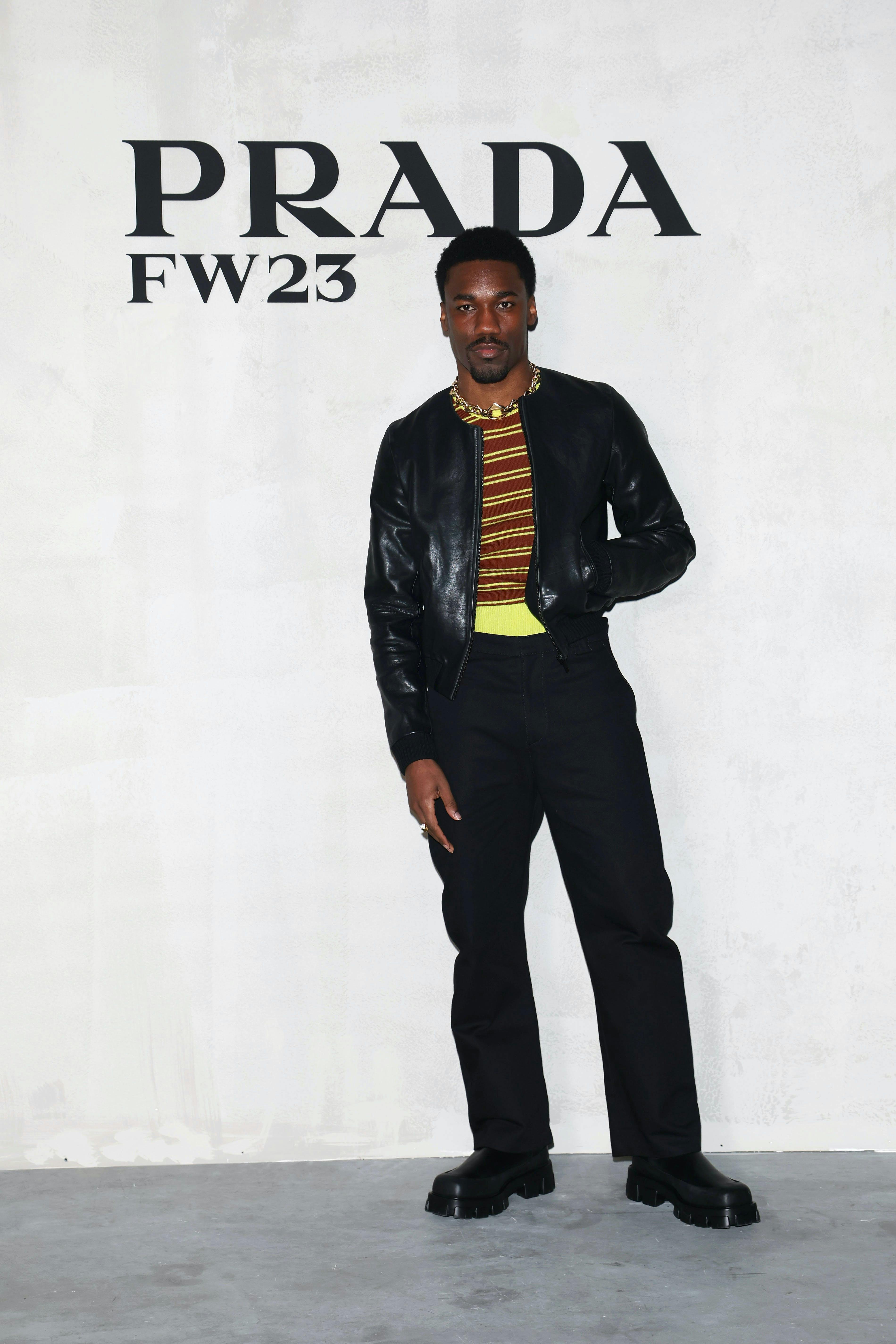 Giveon wears a yellow and red striped top with a black jacket on top and black pants as he attends the Prada show at Milan Fashion Week 2023.