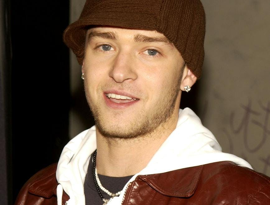 Justin Timberlake wears brown cap, white hoodie, and brown leather jacket.