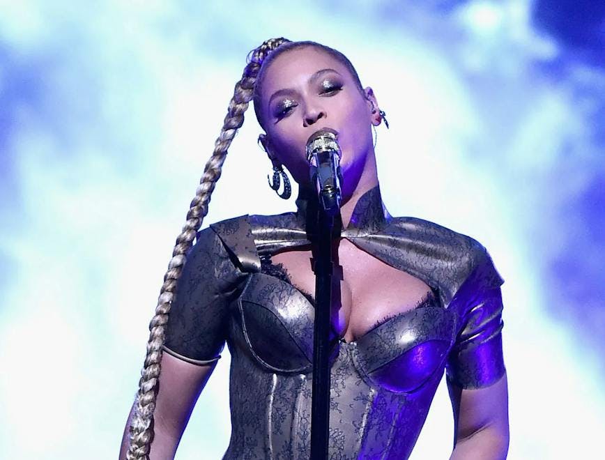 Beyonce on stage with long braid, silver body suit, and knee-high boots.